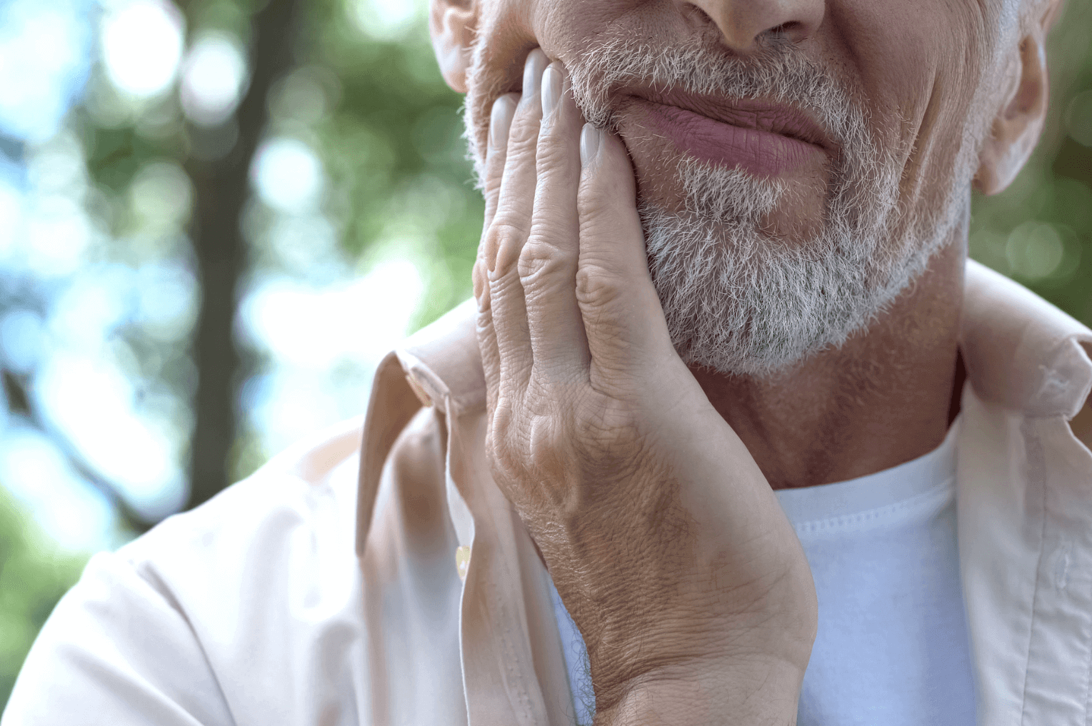 an elderly man holding his cheek in pain from tooth erosion