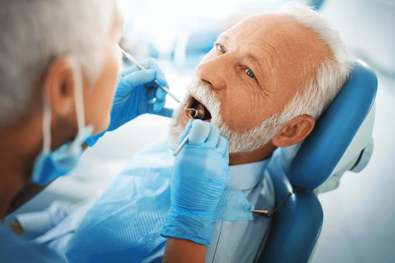 A dentist checking and elderly man's teeth at the dentist
