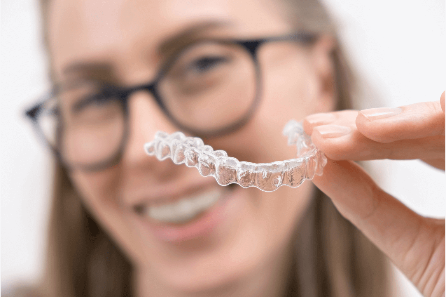 Woman holding clear invisalign aligner close to the camera whilst smiling