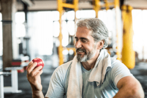 Man at his gym eating an apple with confidence after a dental implant at 19 wimpole street